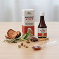 Bottle and box of Balant Kadha 1 Syrup with ingredients on a table